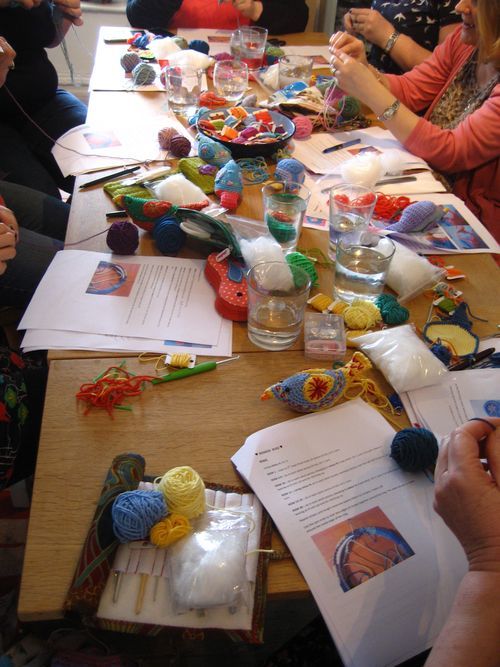 several people sitting at a table with yarn and crochet items on it,