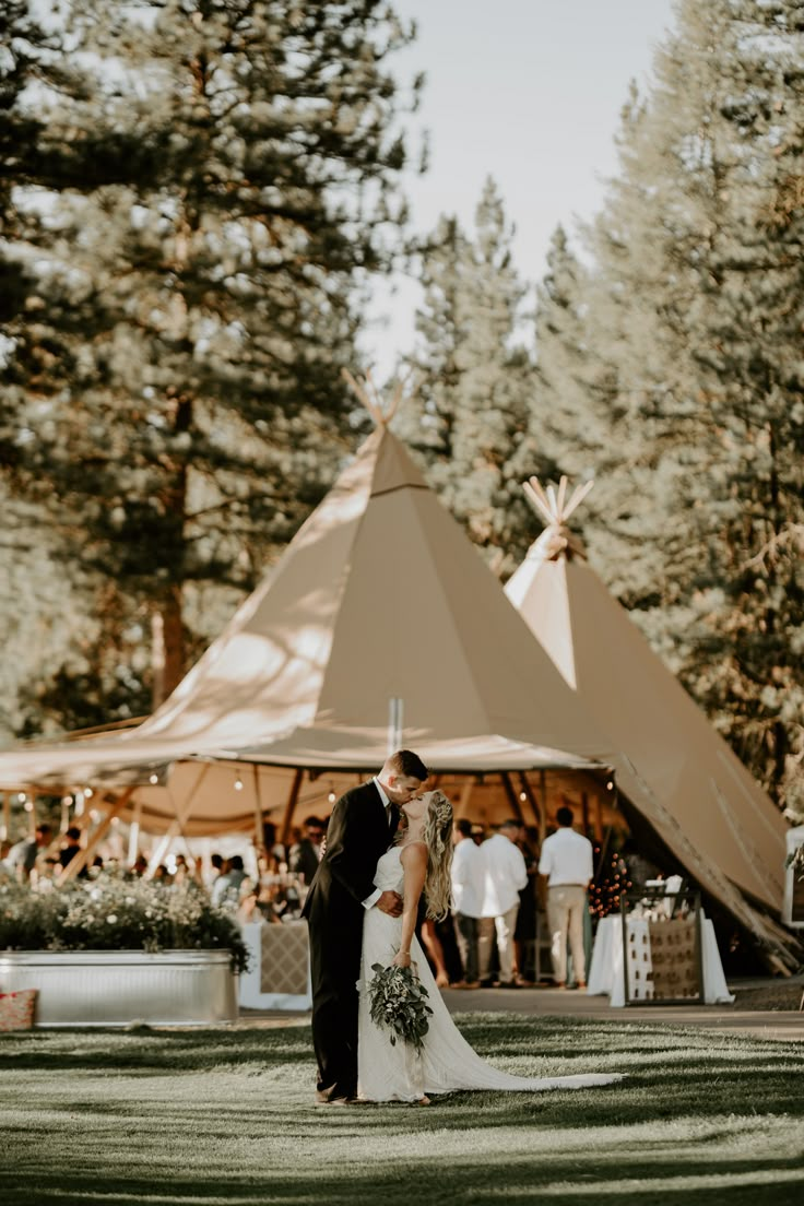 a bride and groom kissing in front of a tippy tent at their wedding reception