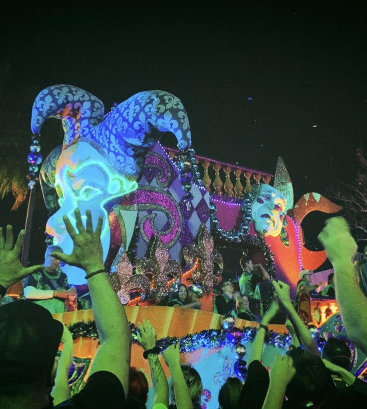 people waving and holding their hands up in front of an elaborately decorated float at night