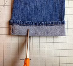 a pair of orange handled scissors on top of a blue jean skirt with holes in it