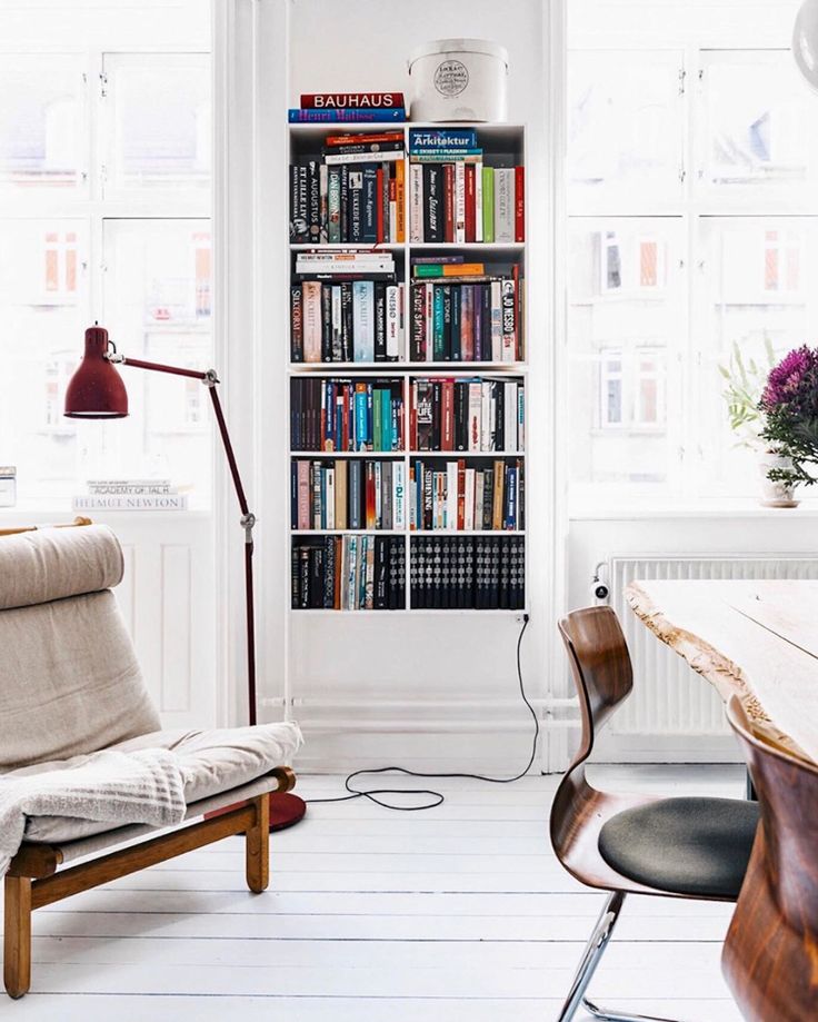 a living room filled with furniture and a book shelf next to a chair in front of a window