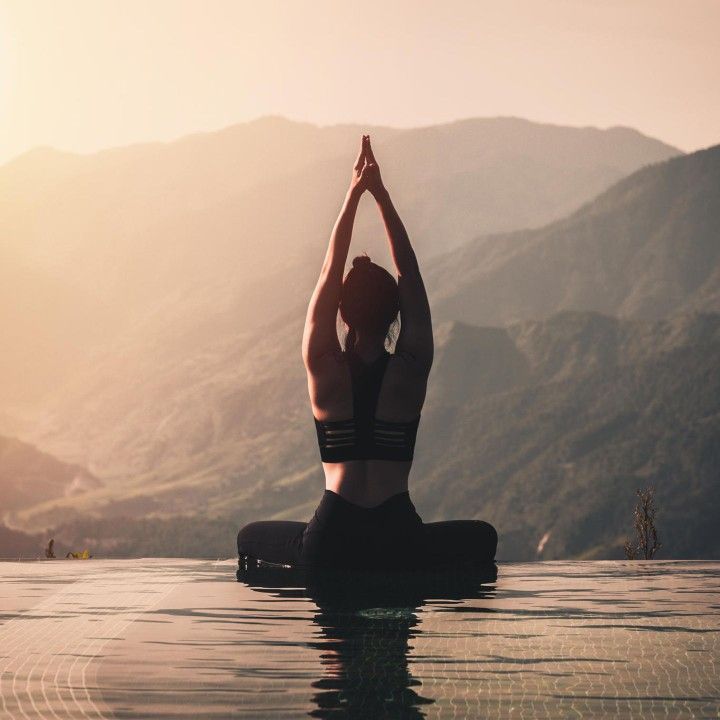 a woman doing yoga in the middle of a pool with mountains in the back ground