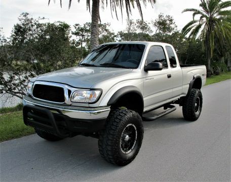 a silver truck parked on the side of a road next to trees and water with palm trees in the background