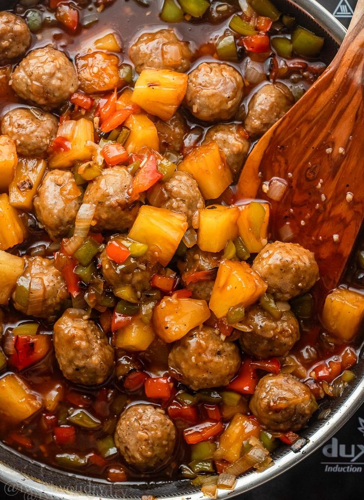 meatballs and vegetables are being cooked in a pot with a wooden spoon on the side