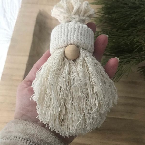 a hand holding a white knitted santa clause ornament with a wooden button