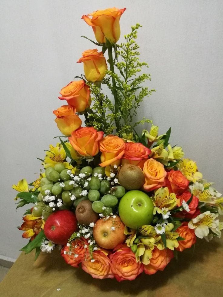 an arrangement of flowers, apples and other fruit in a vase on top of a table