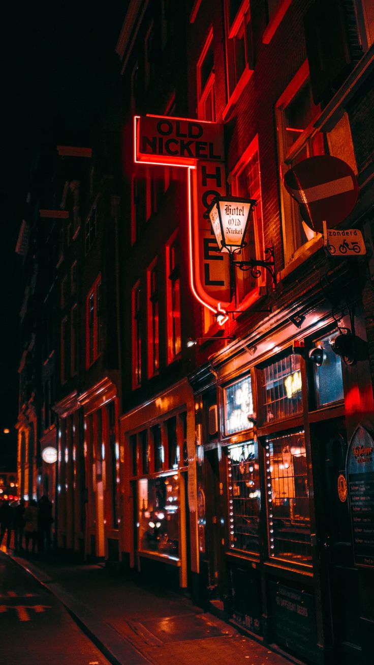 a red neon sign hanging from the side of a building on a city street at night