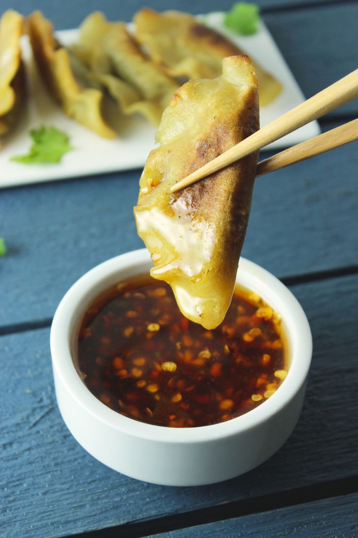 some food is being held up by chopsticks in a bowl with sauce on the side