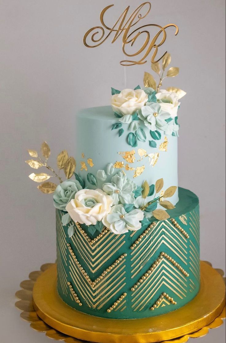 a blue and gold wedding cake with white flowers on the top, sitting on a table