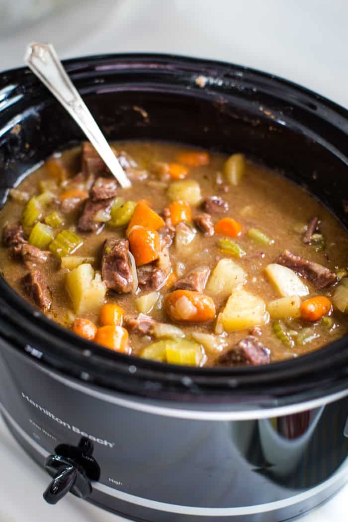 a crock pot filled with beef stew and potatoes on top of a white table