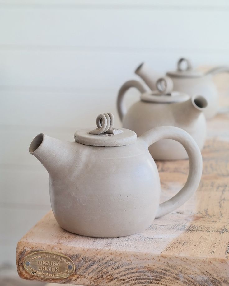 three white teapots sitting on top of a wooden table next to each other