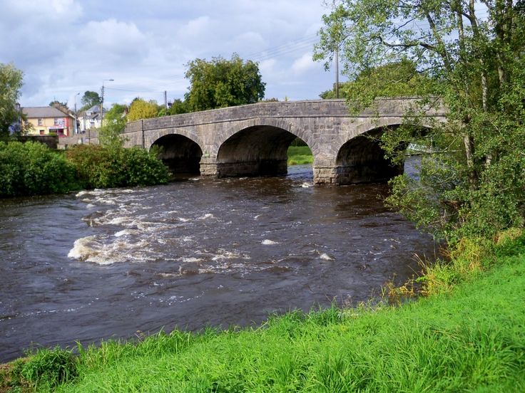 a stone bridge over a river with water rushing under it and green grass in the foreground