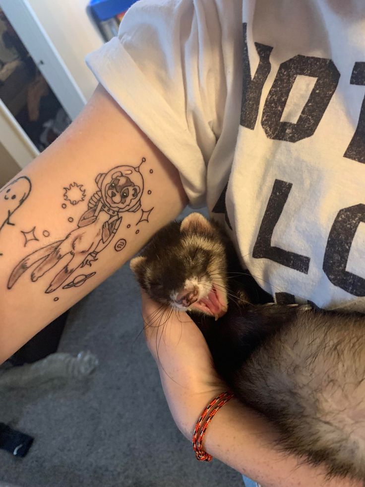 a person holding a small ferret in their arm with tattoos on it's arms