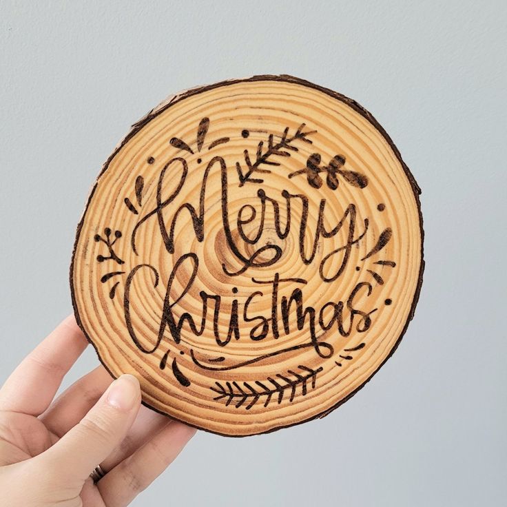 a hand holding up a wooden christmas ornament with the words merry christmas written on it