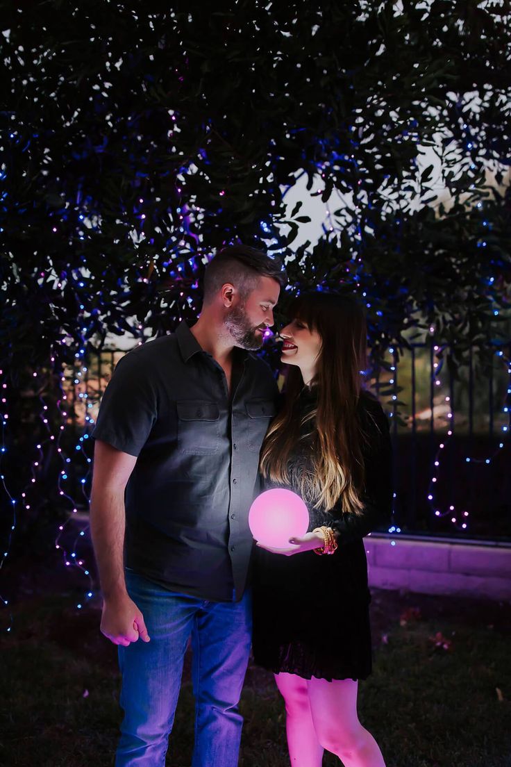 a man and woman standing next to each other in front of a tree with blue lights