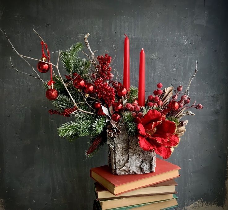 a vase filled with red flowers sitting on top of a stack of books next to candles