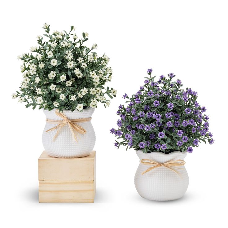 two white vases with purple and white flowers in them, one is tied with a bow