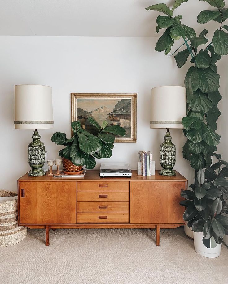 a living room with plants and lamps on the sideboard