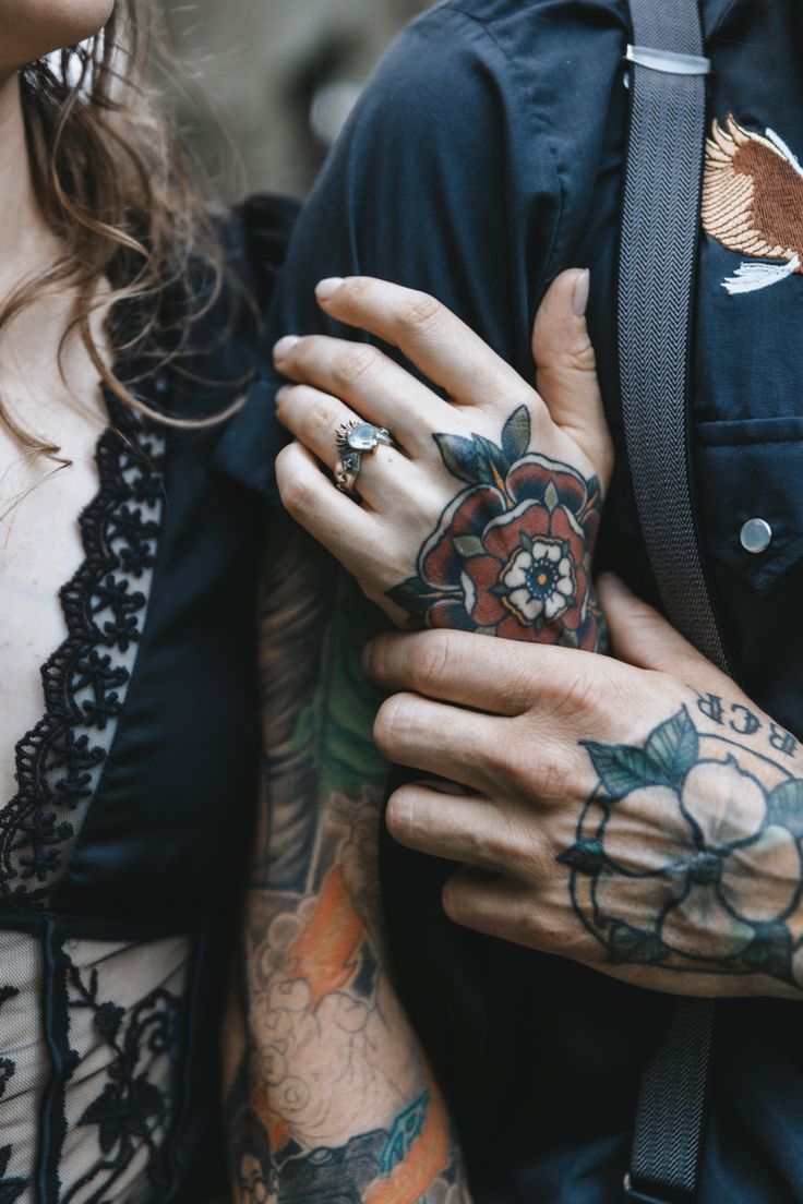 two people with tattoos on their arms holding each other and looking at something in the distance