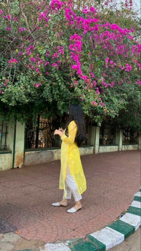 a woman in yellow is walking down the street with pink flowers on trees behind her