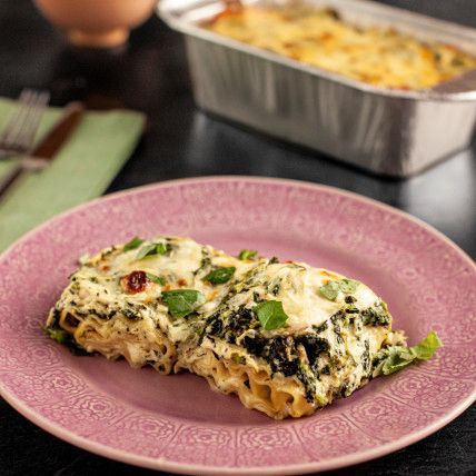 a pink plate topped with lasagna covered in cheese and spinach next to an egg