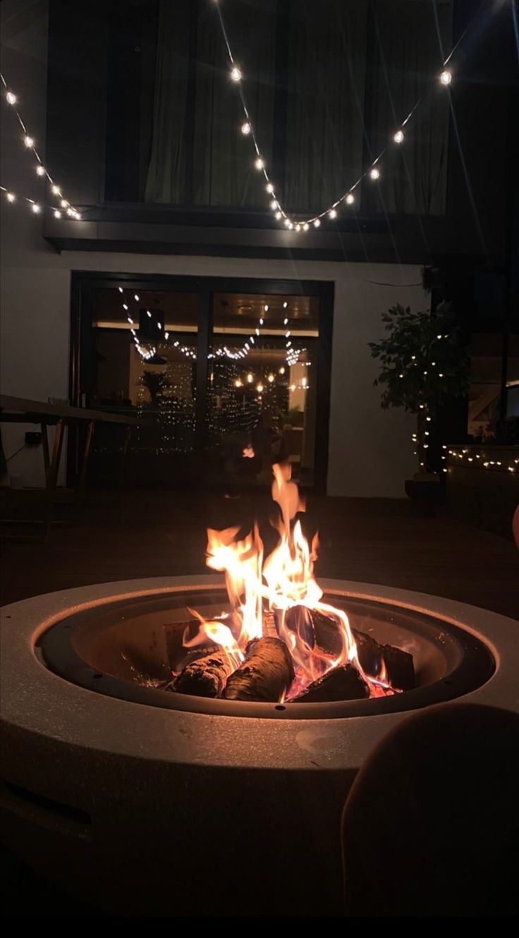 a fire pit is lit up at night with string lights strung across the room and outside