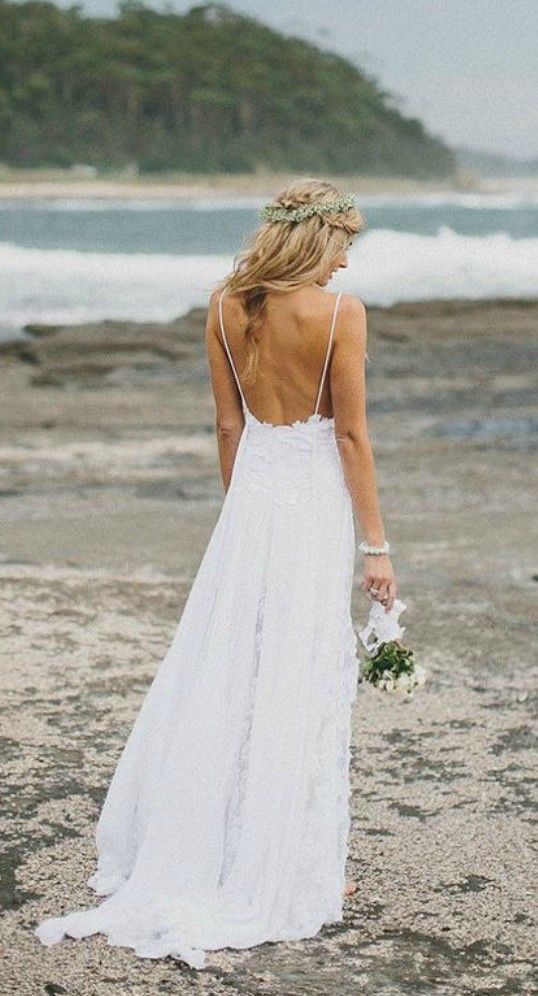 a woman in a white dress standing on the beach with her back to the camera