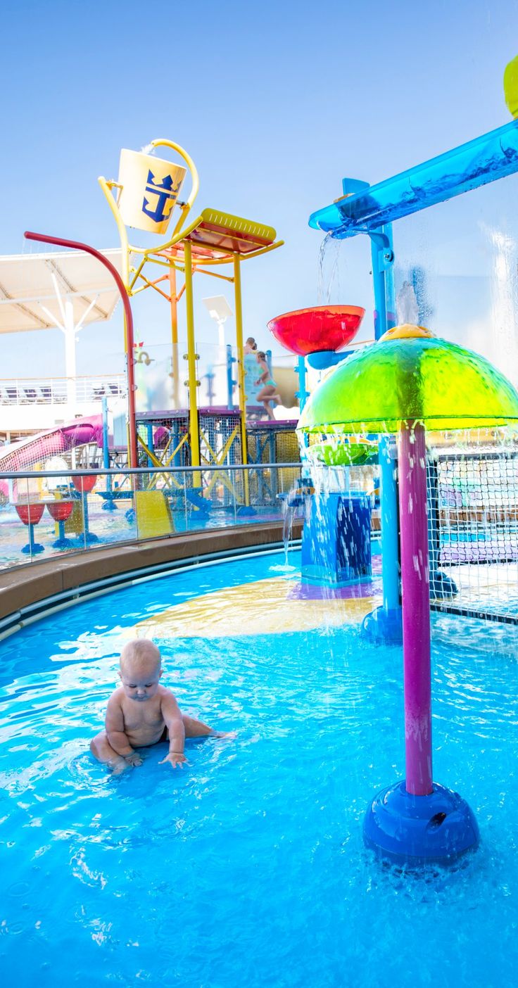 a baby is playing in the pool with an umbrella and water slides behind him on a sunny day