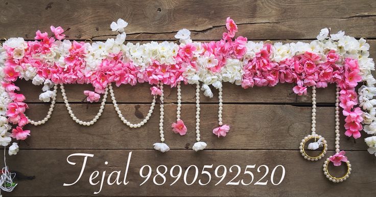 pink and white flowers are hanging on the side of a wooden wall with pearls attached to it