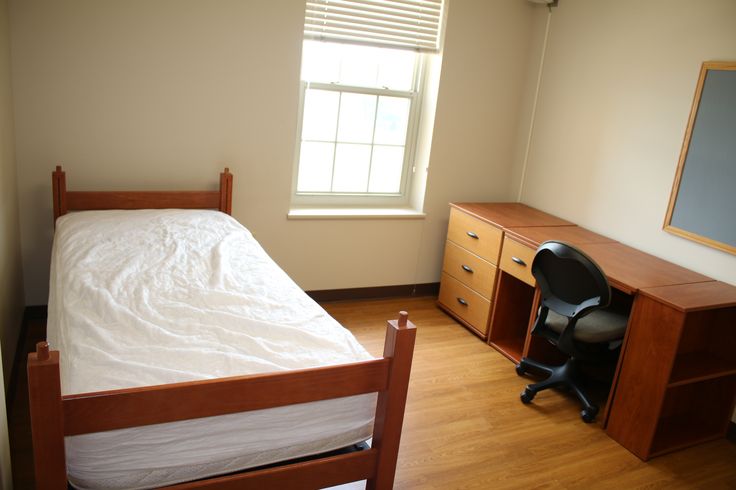 an empty bedroom with a bed, desk and chair next to a window in the corner