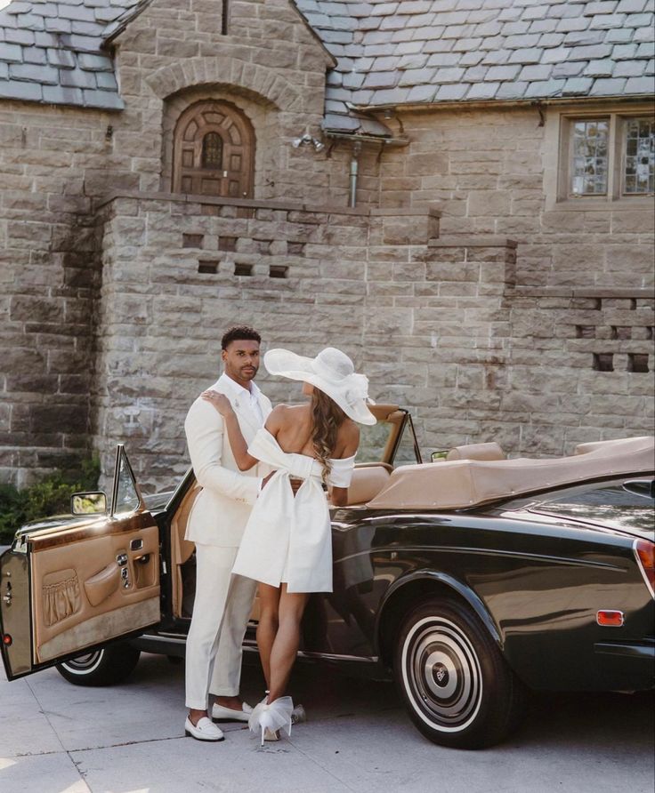 a man and woman standing in front of a car with the door open, dressed in white