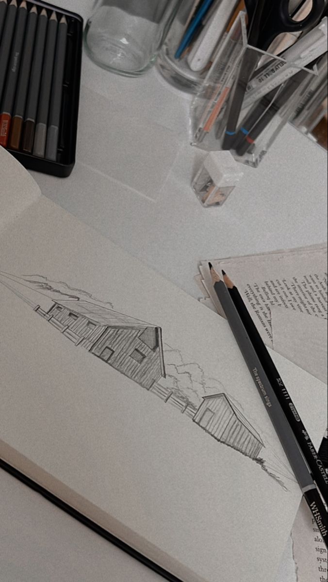 pencils and markers are on the table next to an open notebook with a drawing of a house