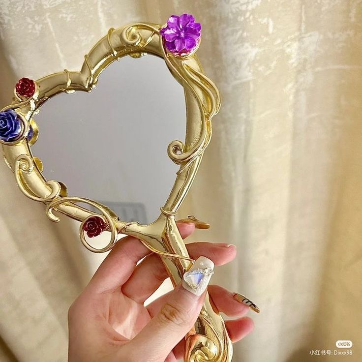 a person holding up a gold heart shaped mirror with flowers on the front and sides