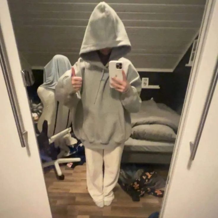 a person taking a selfie while wearing a hoodie and sweatpants in a bedroom