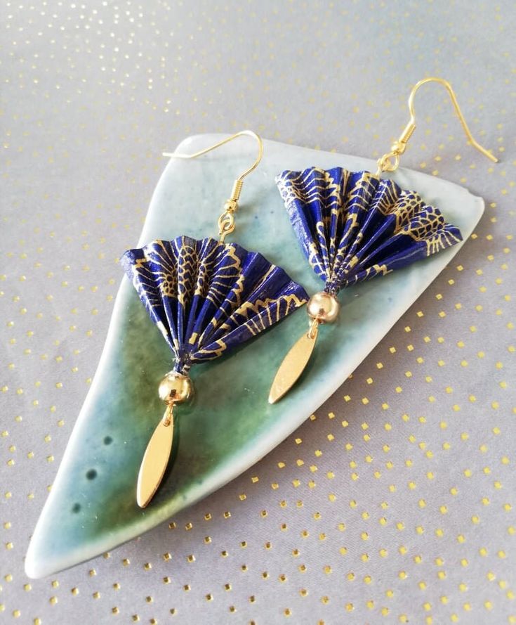 a pair of blue and gold fan shaped earrings on a green plate with polka dots