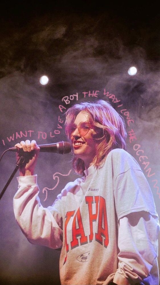 a woman holding a microphone up to her face while standing in front of a stage