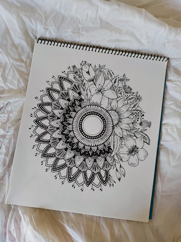 a spiral notebook with an intricate design on the front and back cover sitting on a white sheet