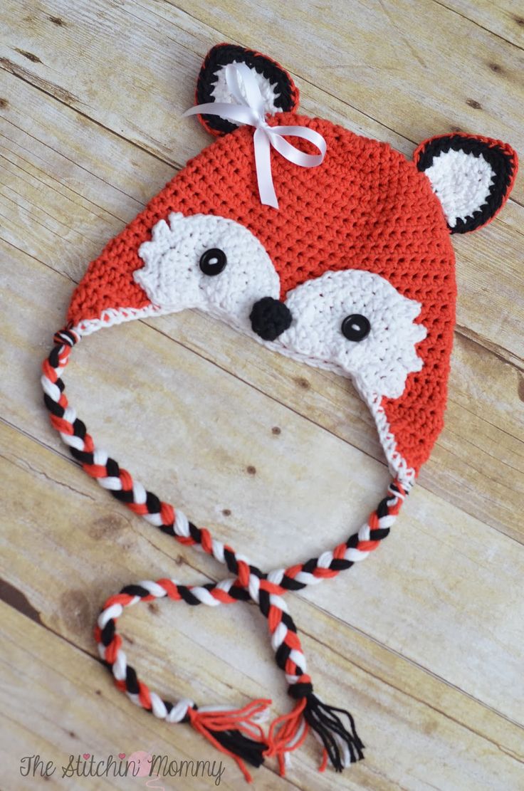 a crocheted red fox hat with ears and tail is laying on a wooden floor