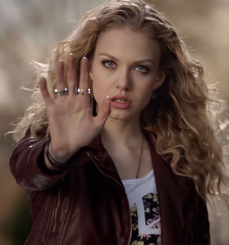 a woman holding her hand up in the air while wearing a brown jacket and white t - shirt