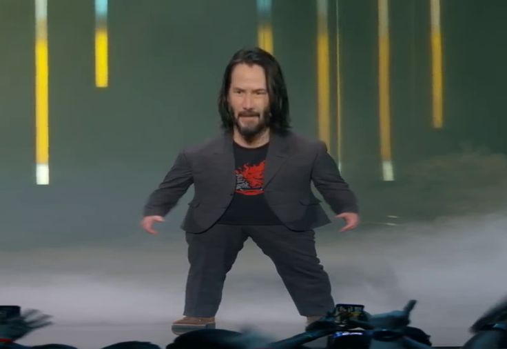 a man with long hair and beard standing on stage in front of an audience wearing a suit