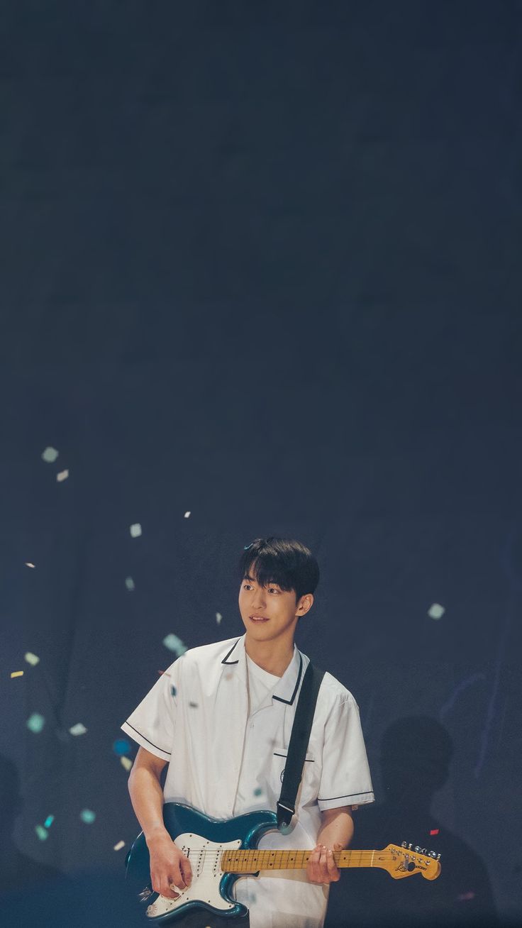 a young man playing an electric guitar in front of confetti falling from the sky