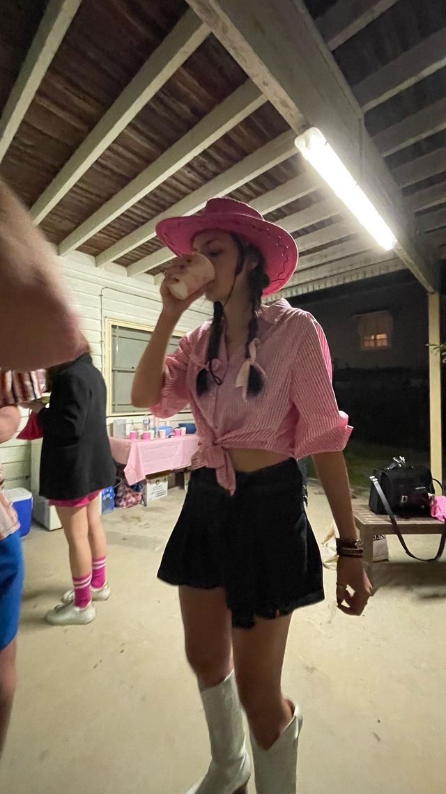 a woman wearing a pink hat and black skirt standing in front of a table with food on it