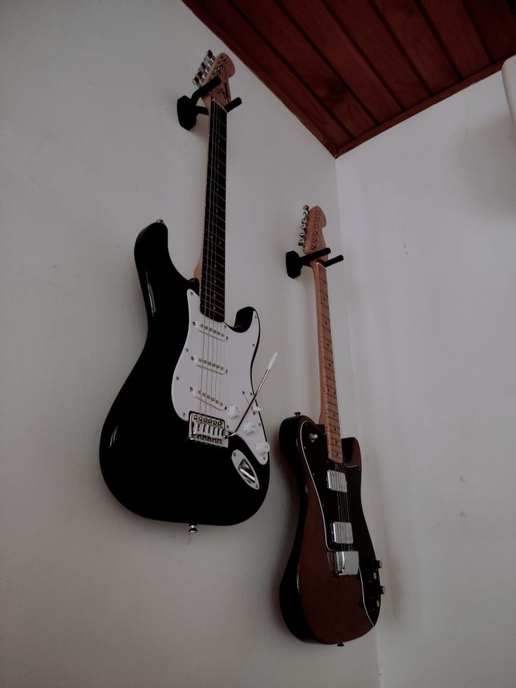 two guitars are hanging on the wall next to each other, one black and one white