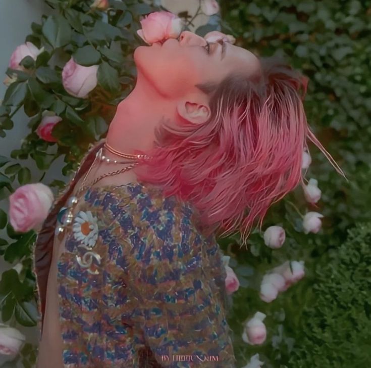 a woman with pink hair standing in front of flowers