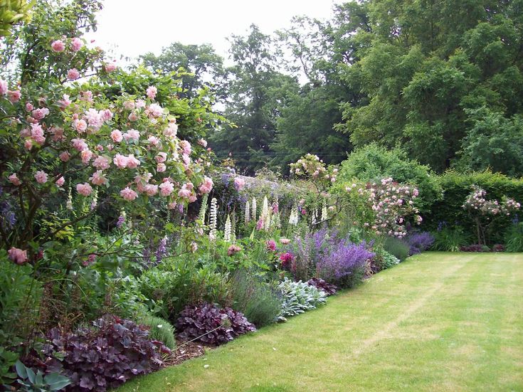 a lush green lawn surrounded by lots of purple and white flowers on the side of it