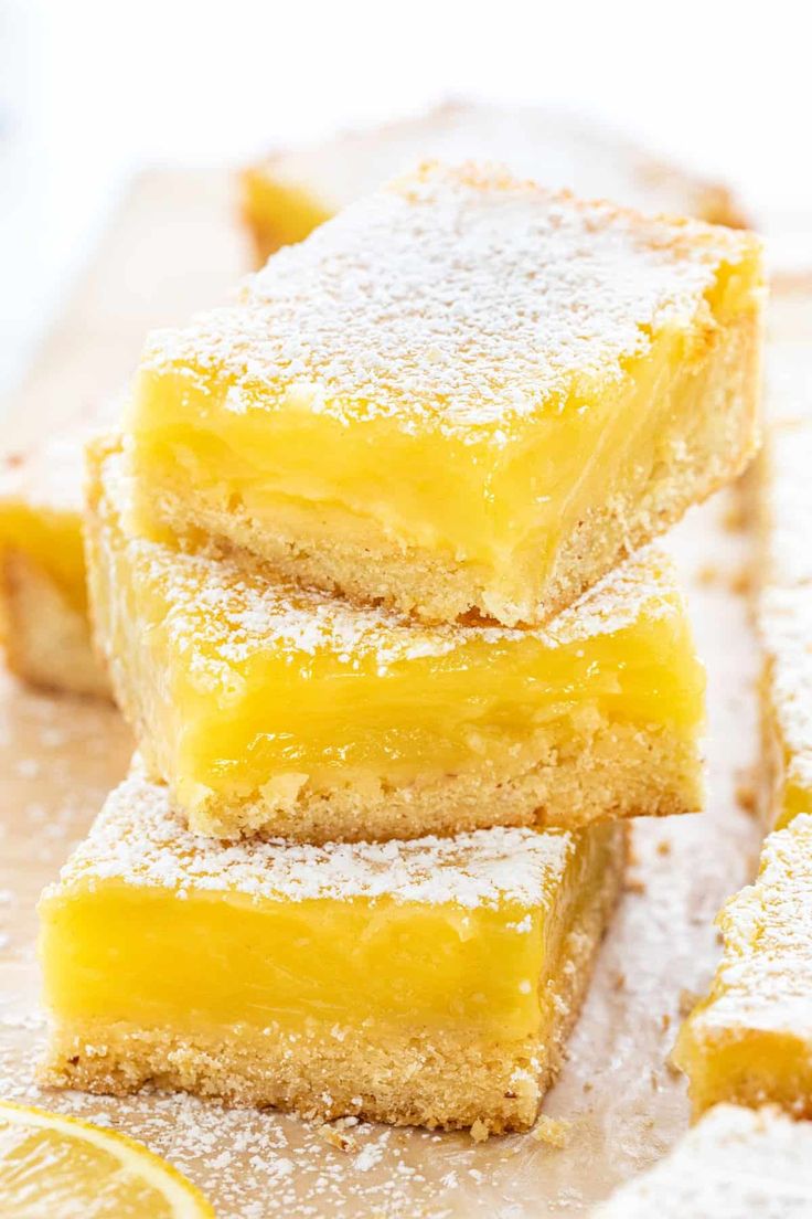 three lemon bars stacked on top of each other with powdered sugar and two lemons in the background