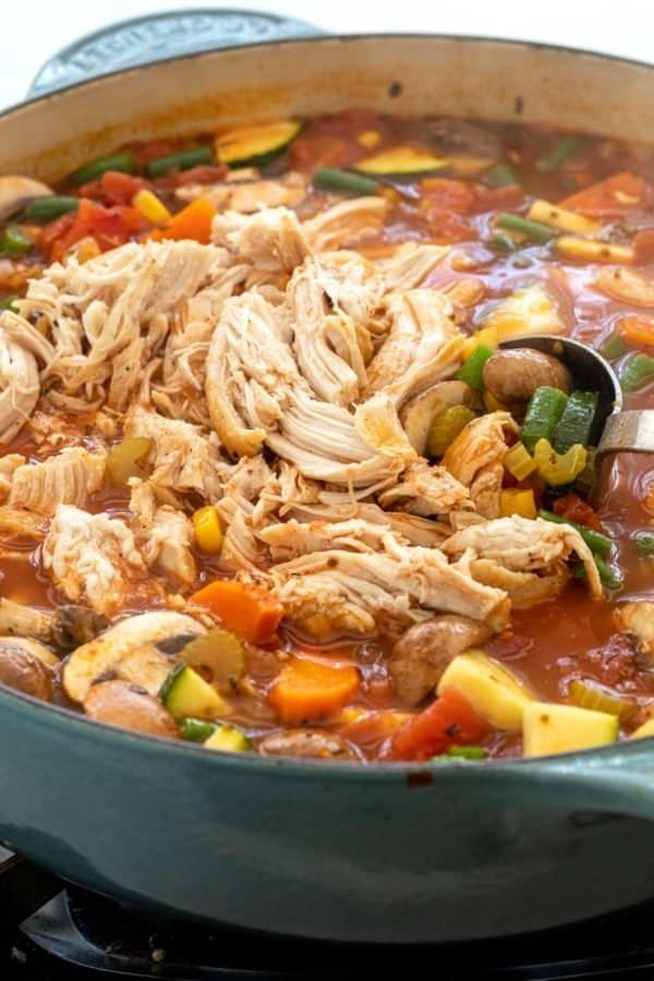 a pot filled with chicken and vegetable soup on top of a stove burner next to a wooden spoon