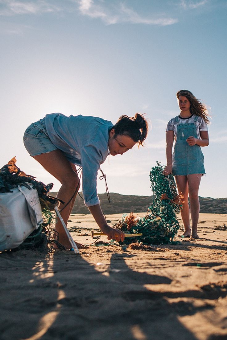 two women are standing in the sand and one is holding a shovel