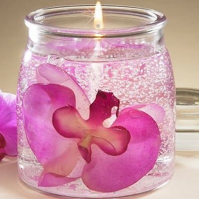 a candle that is inside of a glass jar with pink flowers on the inside and bottom