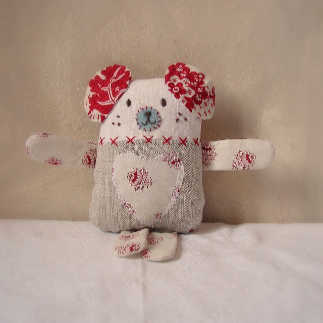 a white stuffed animal with red flowers on it's head and arms, sitting on a bed